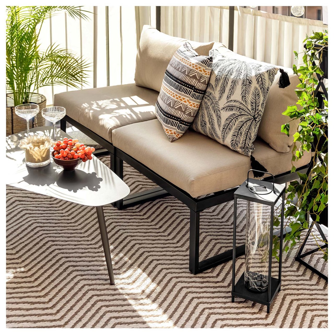 Kleiner, sonniger Lounge-Bereich mit Sofa und Tisch auf einem beigen Teppich.