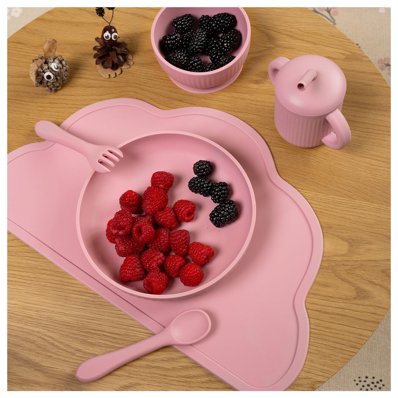 Rosa Kinderservice mit Himbeeren und Blaubeeren auf einem Tisch.