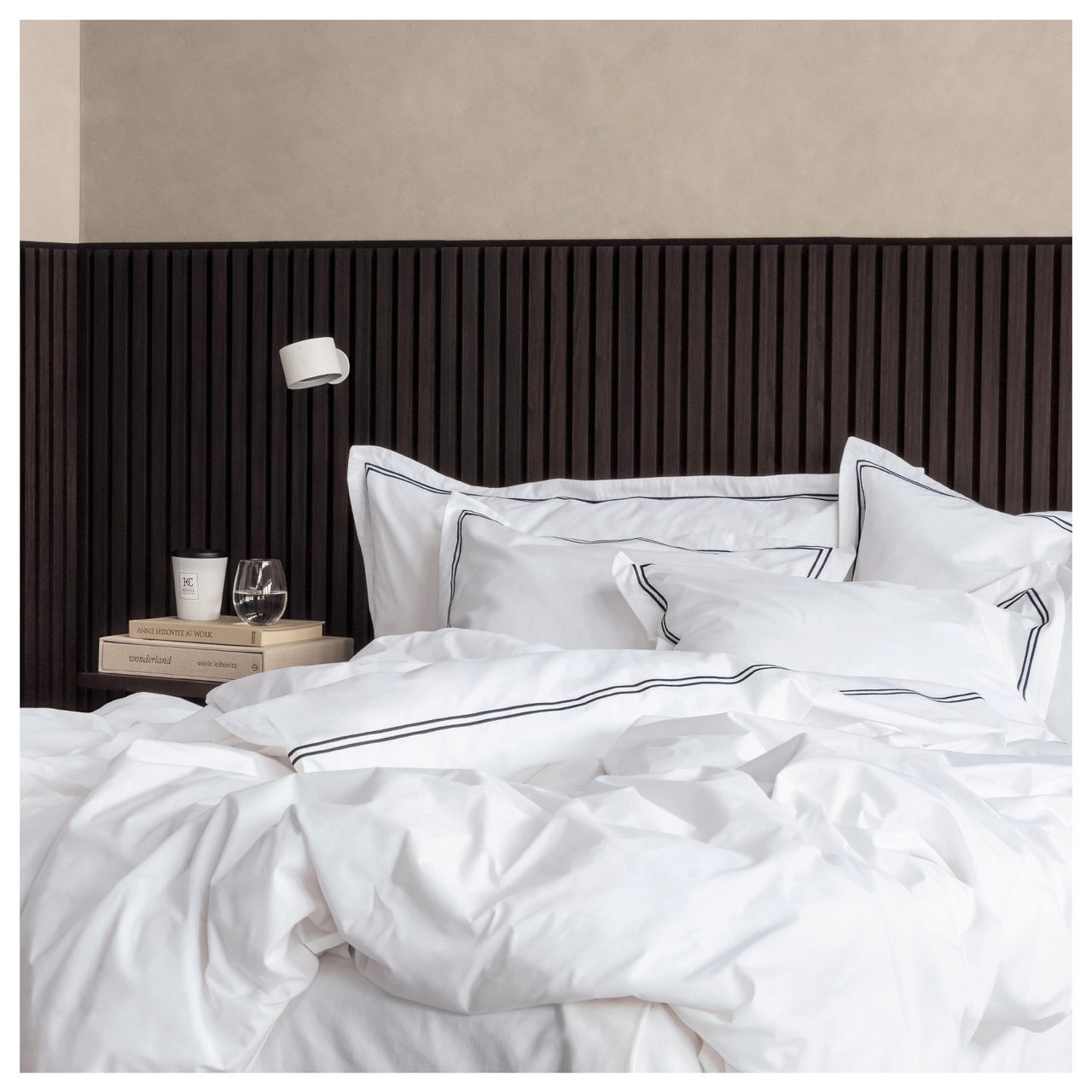 Sovrum med mörk akustikpanel monterad bakom sängen. Säng bäddad i vita påslakan.