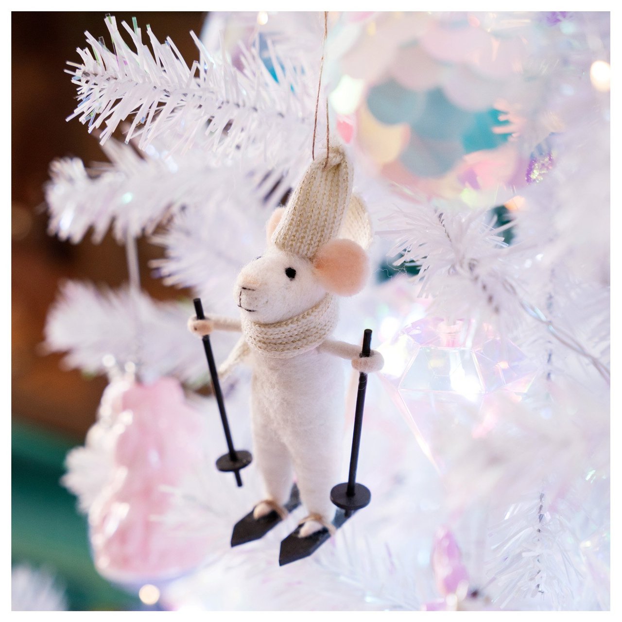 Valkoiseen joulukuuseen on ripustettu hiihtävää hiirtä esittävä joulukoriste.