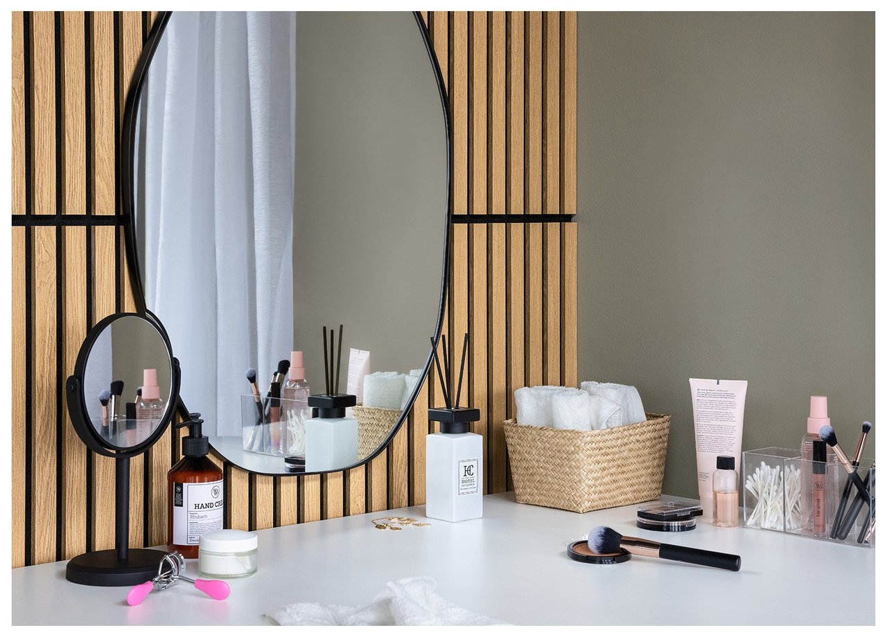 Rund spegel på vägg ovanför ett bord med smink, skönhetsprodukter och en sminkspegel på fot.