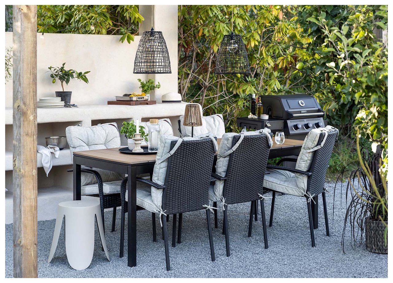 Garten mit Esstisch und schwarzen Stühlen mit hellgrauen Hochlehnenauflagen. Beiger Hocker neben dem Tisch.