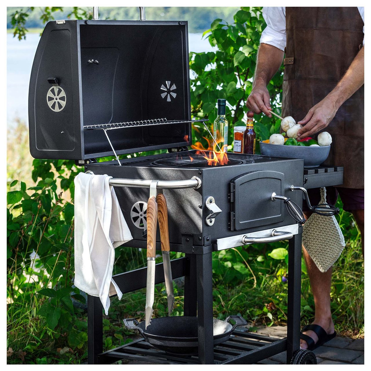 Holzkohlegrill mit Flammen. Jemand steckt Champignons auf einen Spieß.