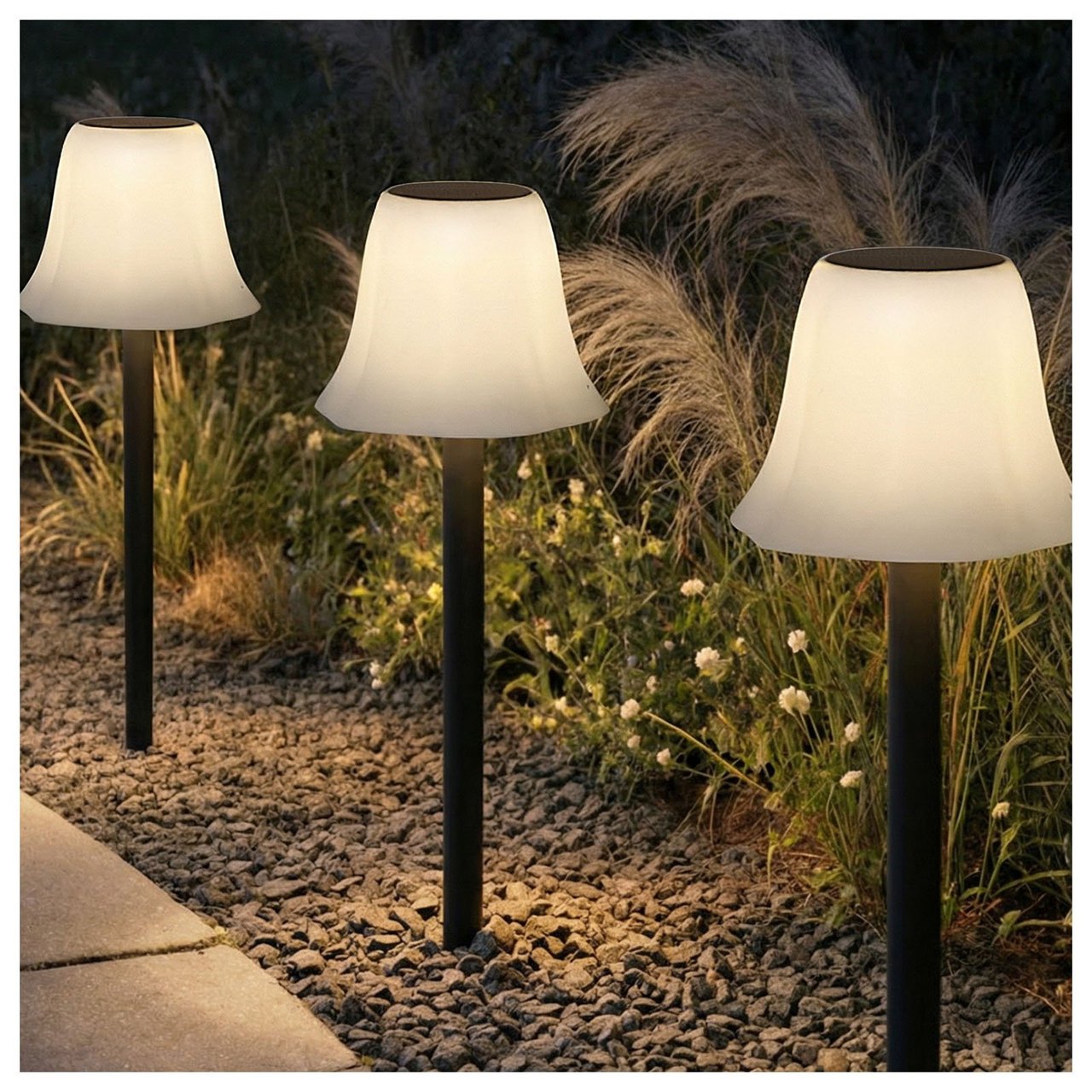 Flere lamper av modellen Hemsön med svart fot og hvit, bølget skjerm stukket ned i grusen ved en hagegang.