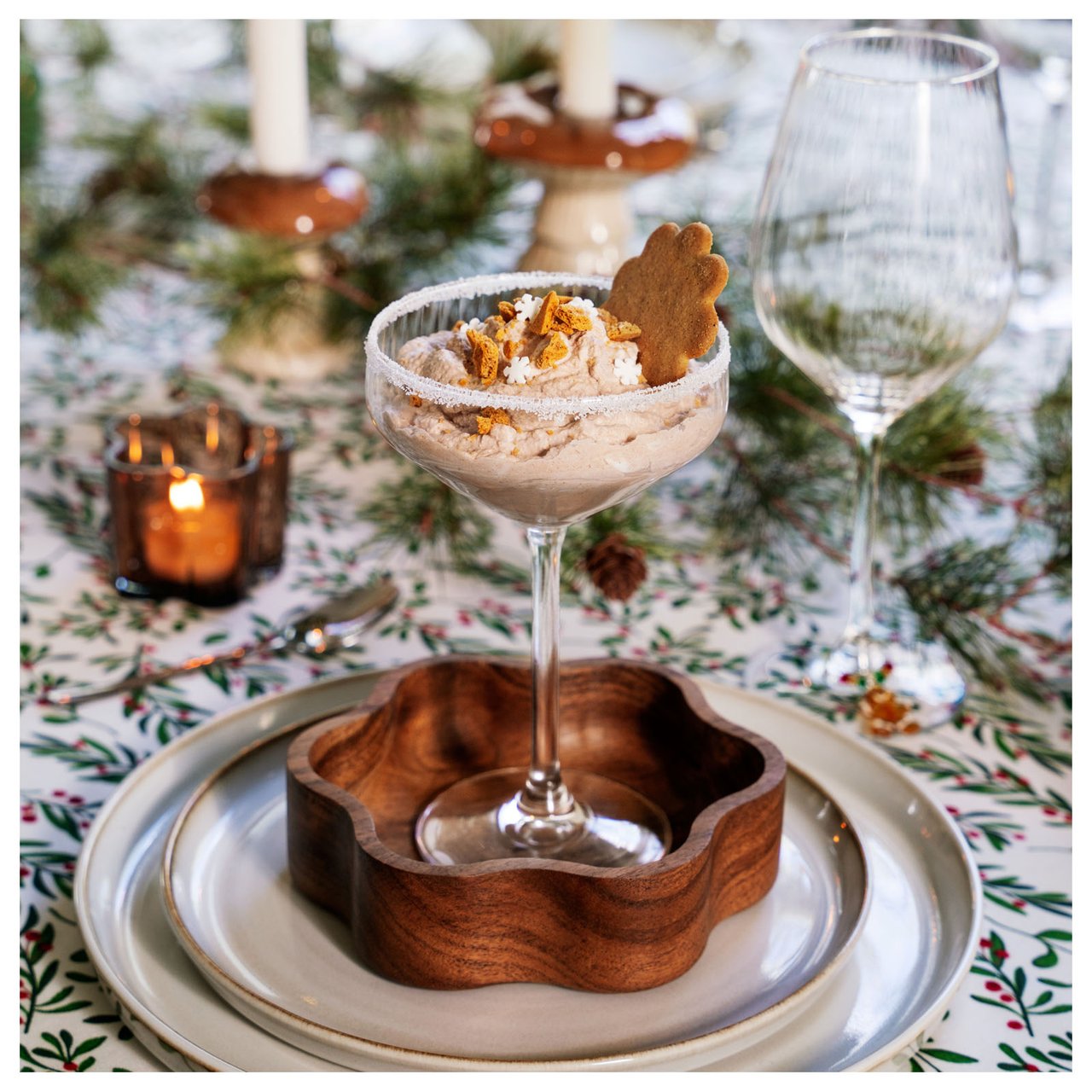 Weihnachtstisch mit grün gemusterter Decke, Dessert im Glas, Holzschalen und Geschirr.