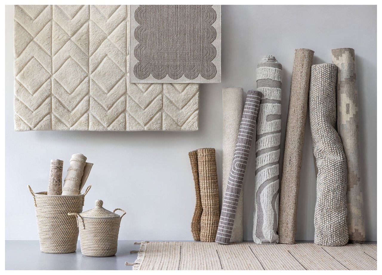 Teppiche in verschiedenen natürlichen Farben und Größen hängen an einer Wand und stehen zusammengerollt nebeneinander.