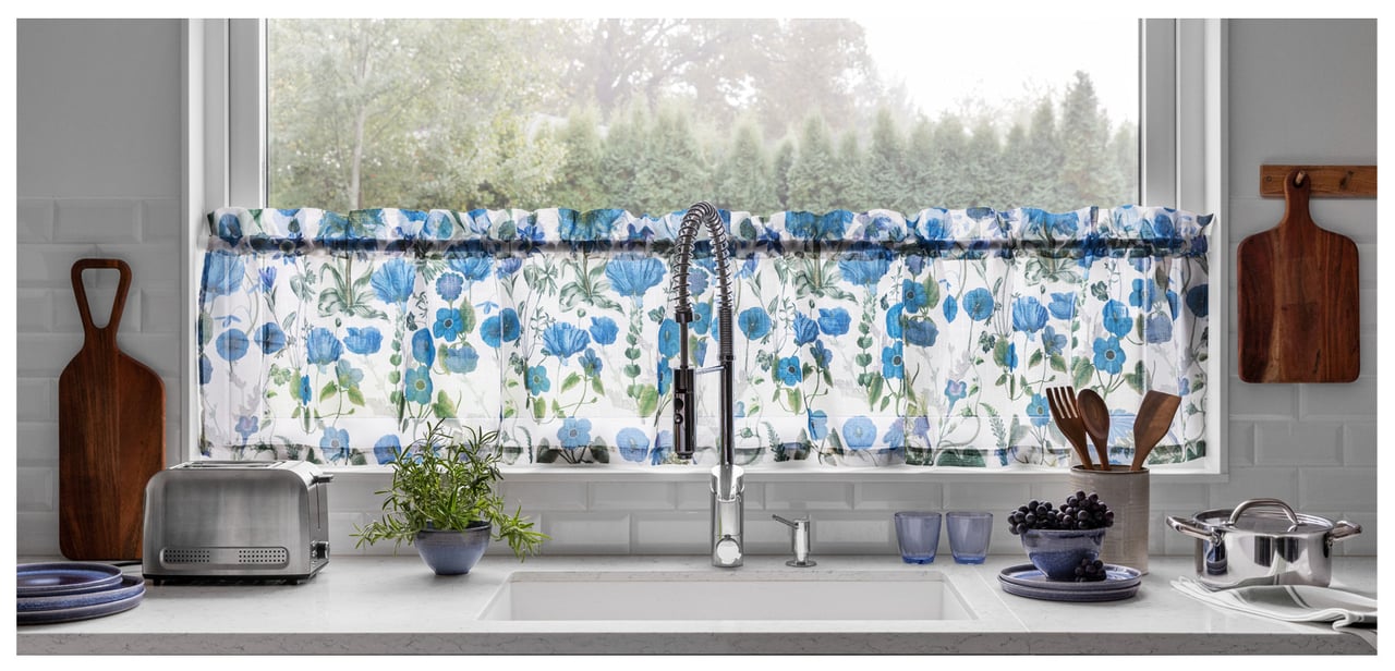 Küche mit Spüle vor einem Fenster mit blauem, kleingeblümtem Querbehang.