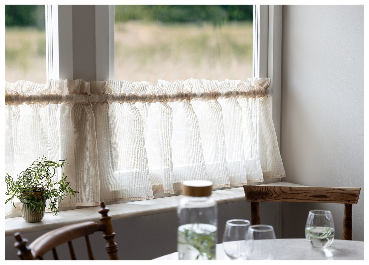 Küchenfenster mit blau geblümtem Querbehang über der Spüle und Arbeitsfläche mit Küchenutensilien.