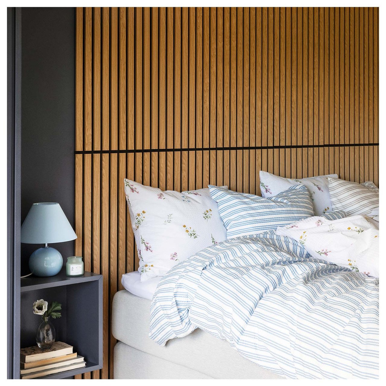 Sovrum där akustikpanel i ek har monterats på väggen bakom sängen. Säng bäddad med påslakan i blommigt och randigt. 