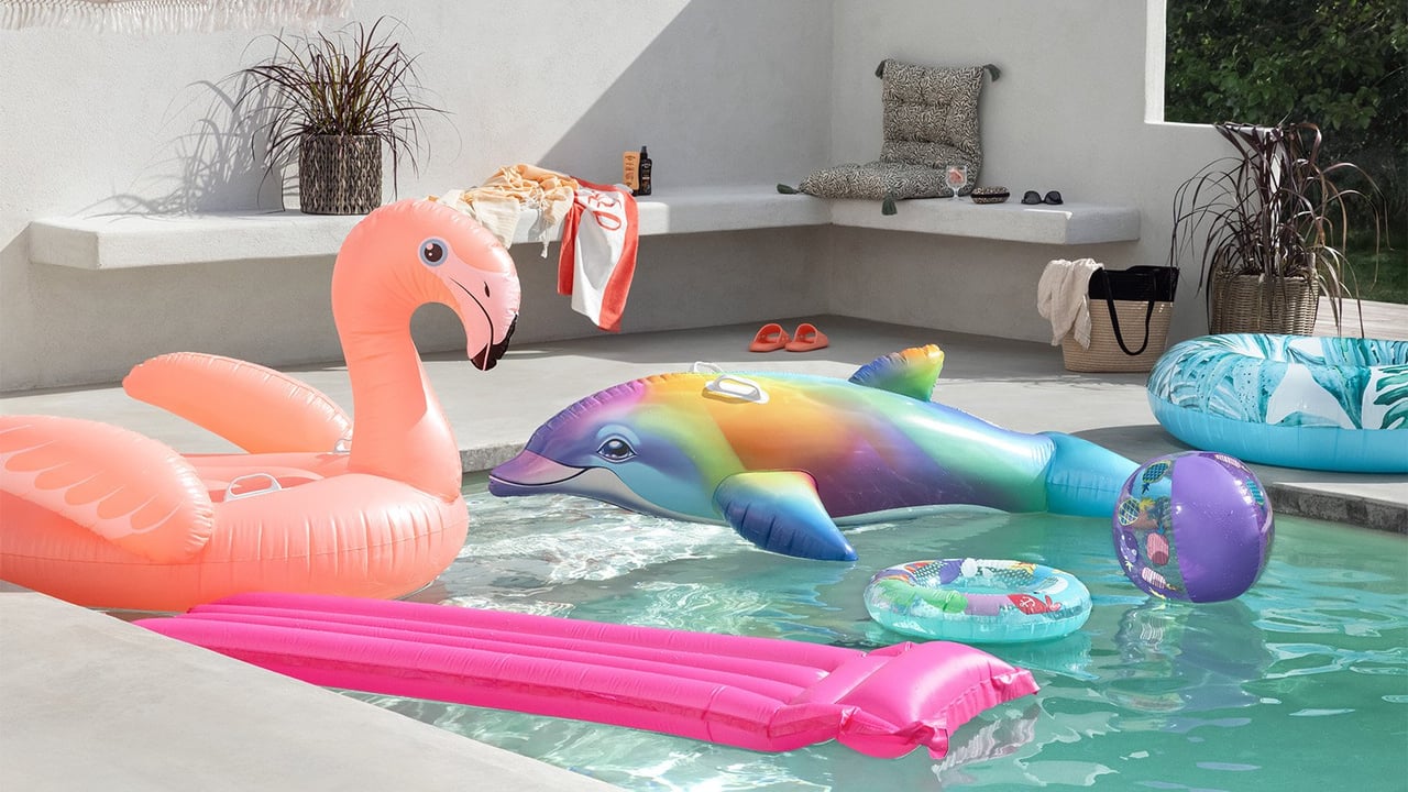 Uteplats vid pool med solsäng, sidobord, växter och badleksak i form av en flamingo.