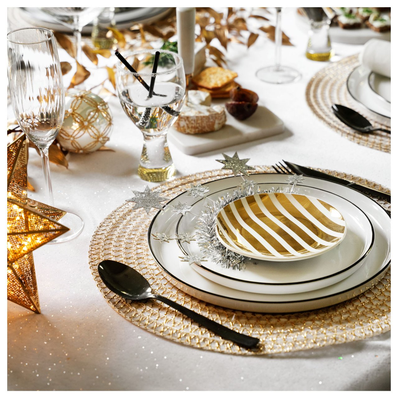 Neujahrstisch in Weiß und Gold mit gestreiftem Teller, Sterndeko und funkelnden Details.