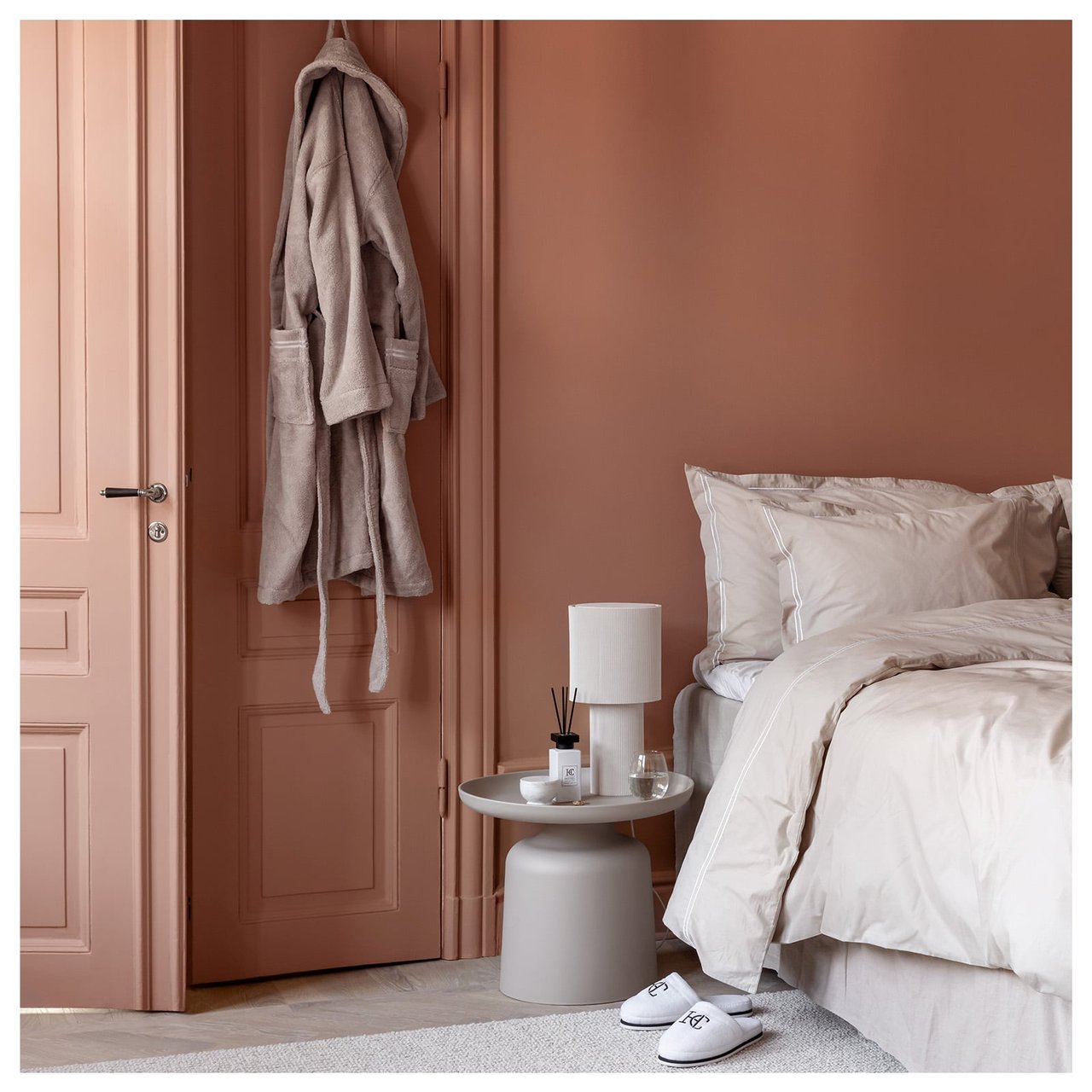 Et soverom med en seng med beige sengetøy. På døren henger en beige morgenkåpe.