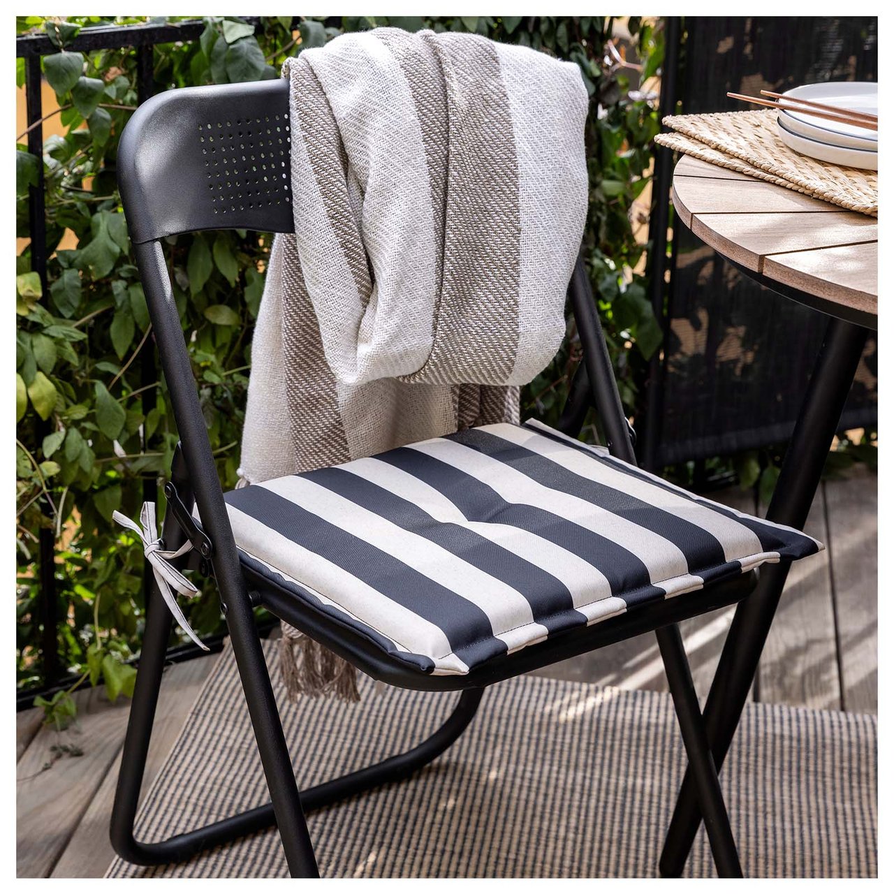 Svart sammenleggbar stol med pute i svarte og hvite striper. På ryggstøtten henger det et pledd.