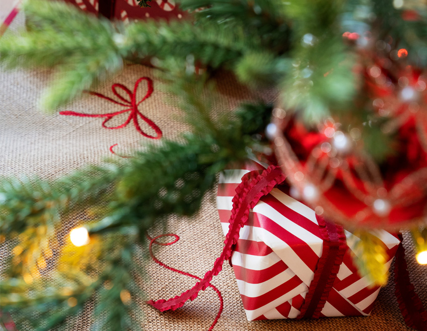 Innpakkede julegaver under juletre pyntet med lys og kuler.