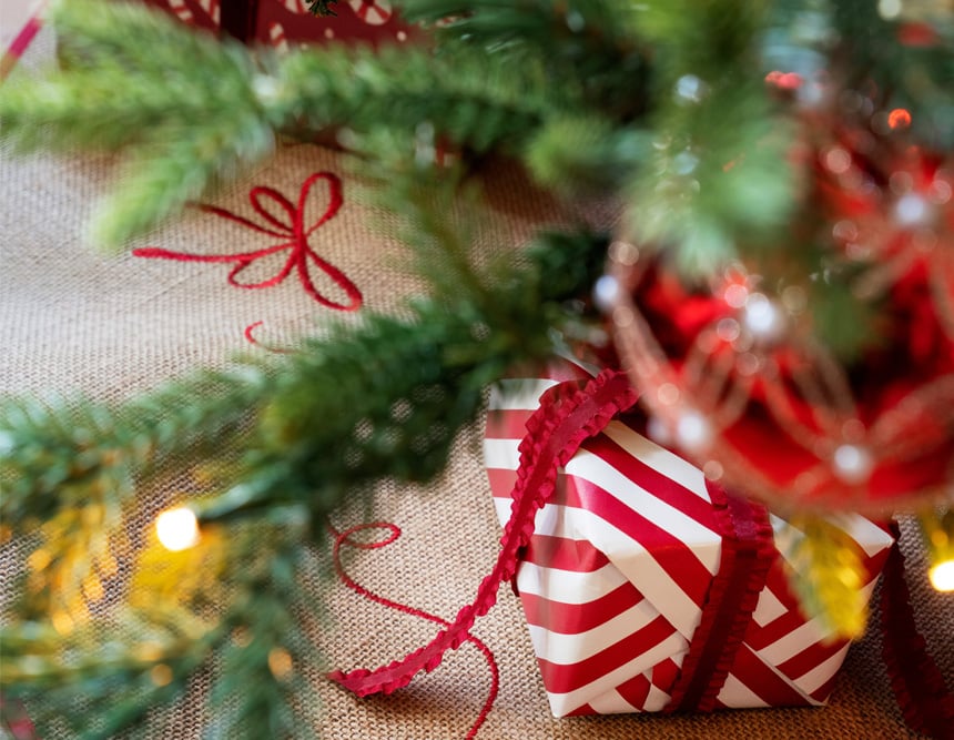 Innpakkede julegaver under juletre pyntet med lys og kuler.