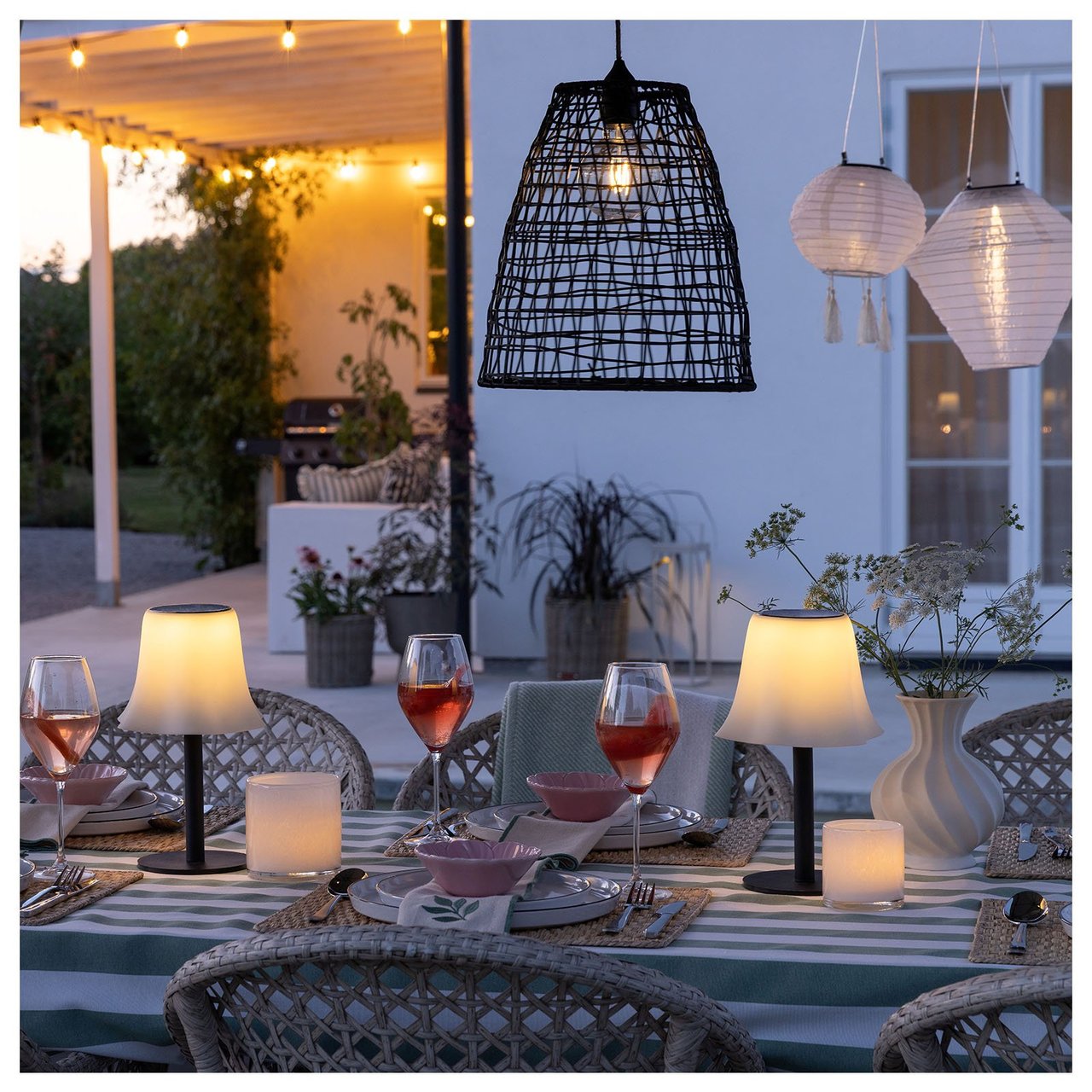 Et dekket bord i kveldslyset på en uteplass. I taket henger det rislamper og en rottinglampe.