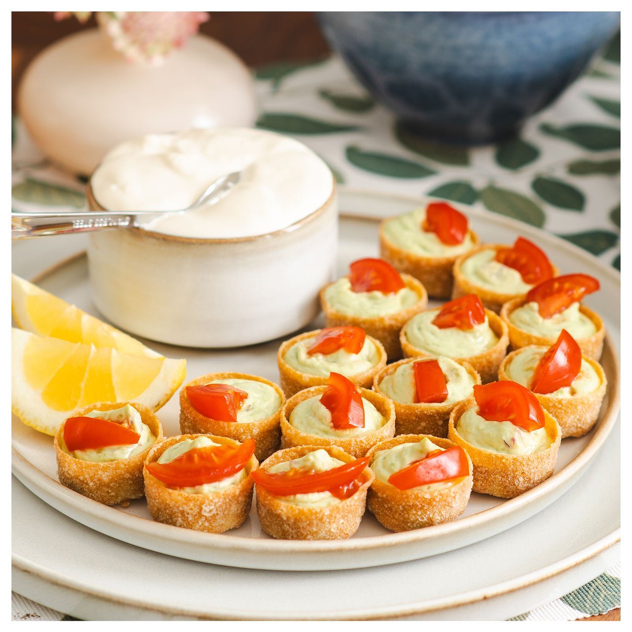 Kleine Krustaden mit Avocadofüllung und Tomate, serviert mit Zitrone und Dipp auf einem Teller.