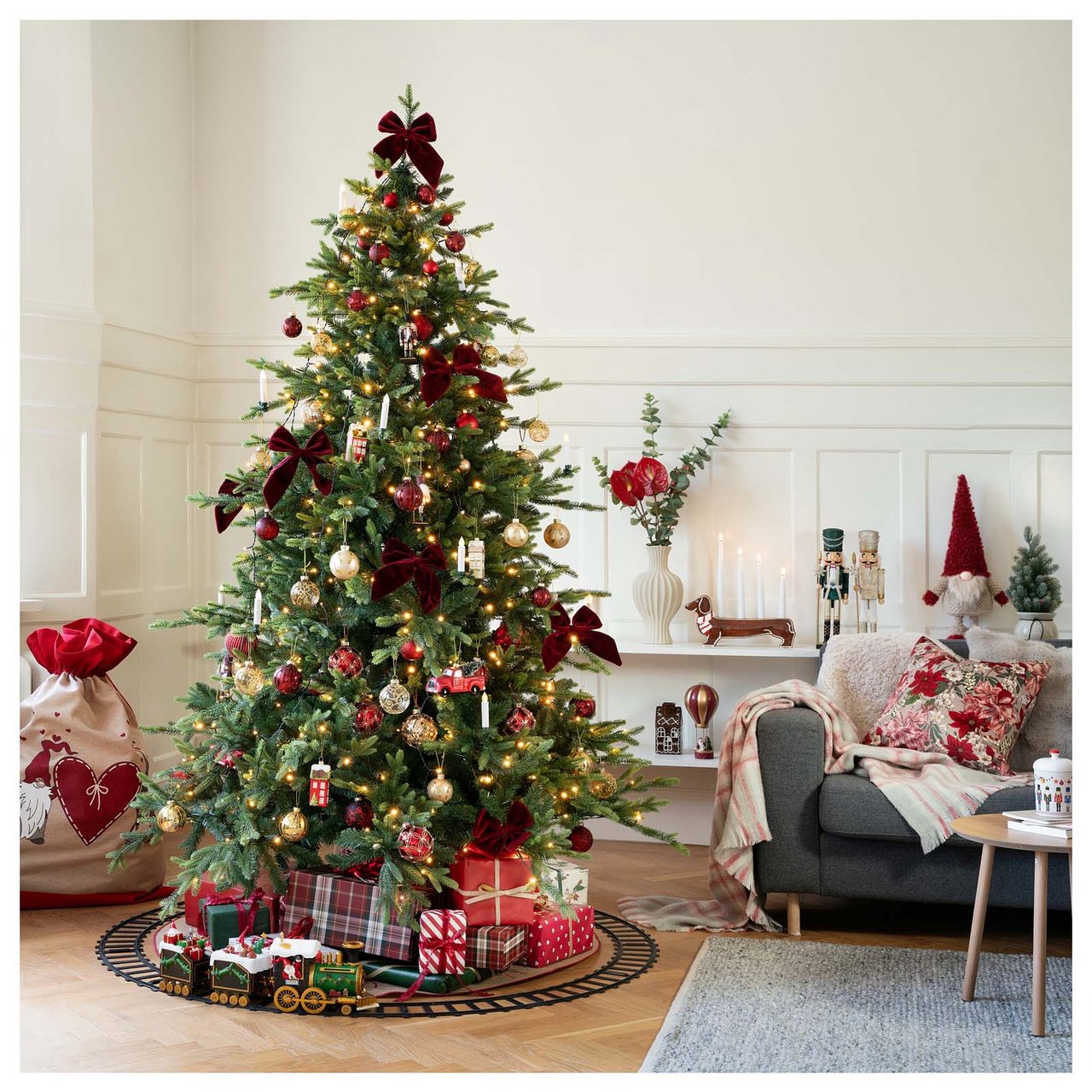 Großer Kunstbaum mit rotem und goldenem Schmuck in einem festlich dekorierten Wohnzimmer.