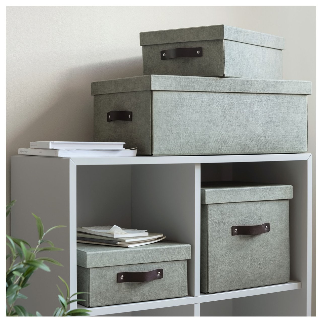 Grüne Aufbewahrungsboxen unterschiedlicher Größe, die in und oben auf einem weißen Bücherregal stehen.