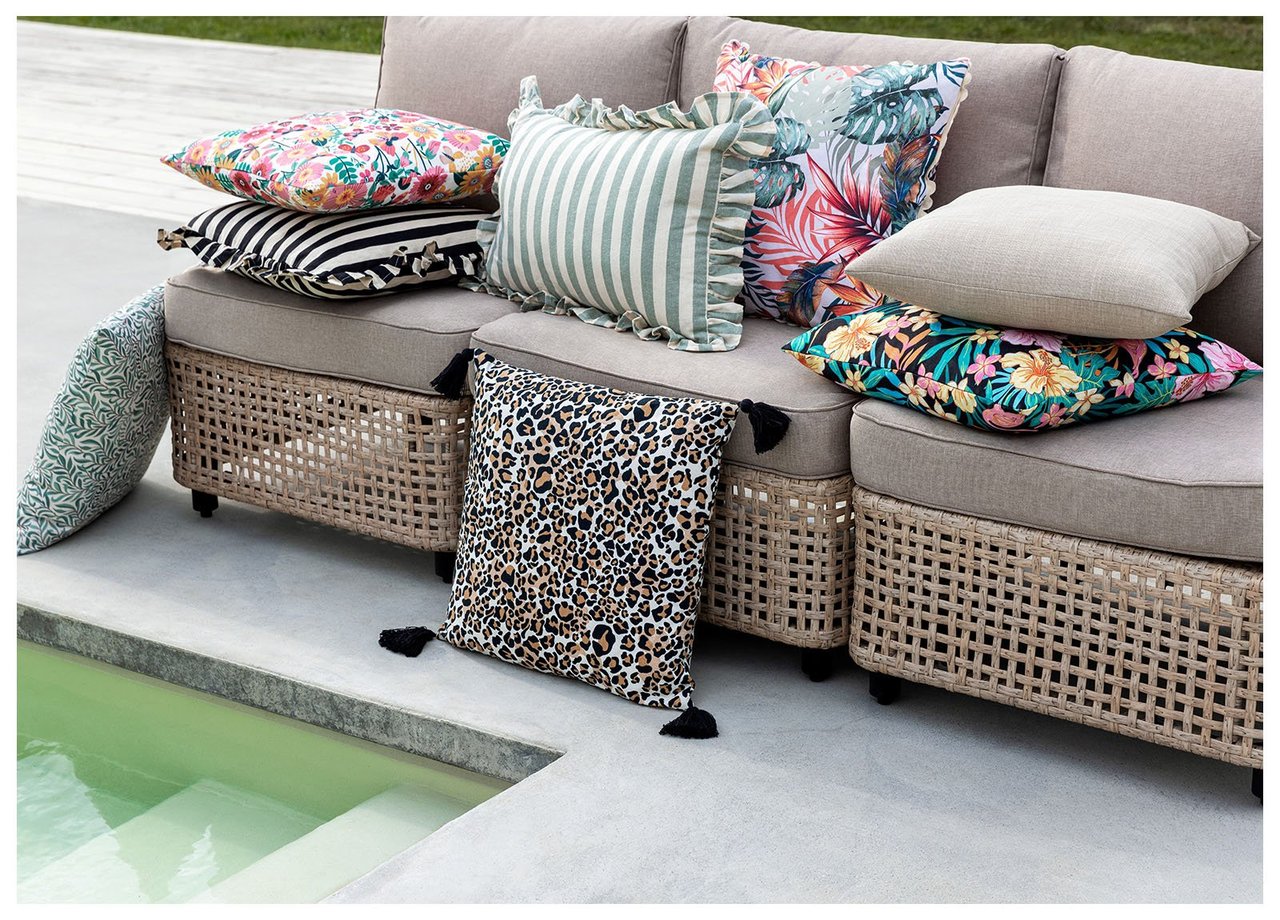 Outdoor-Kissen in verschiedenen Mustern und Farben liegen auf einem Loungesofa neben einem Pool.