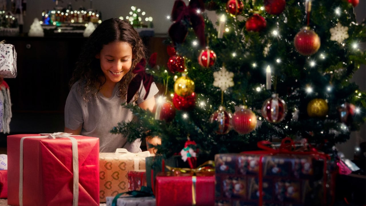 Tonårstjej öppnar julklappar vid en pyntad julgran i ett stämningsfullt vardagsrum.