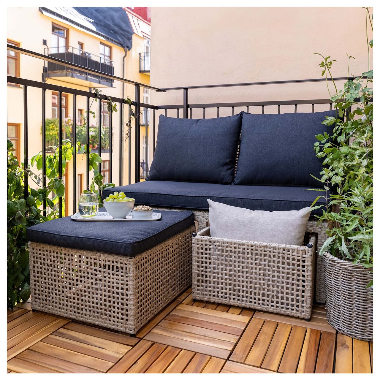 Kleines beiges Loungesofa aus Kunstrattan mit Stauraum in der Ecke eines Stadtbalkons zusammen mit vielen grünen Pflanzen.