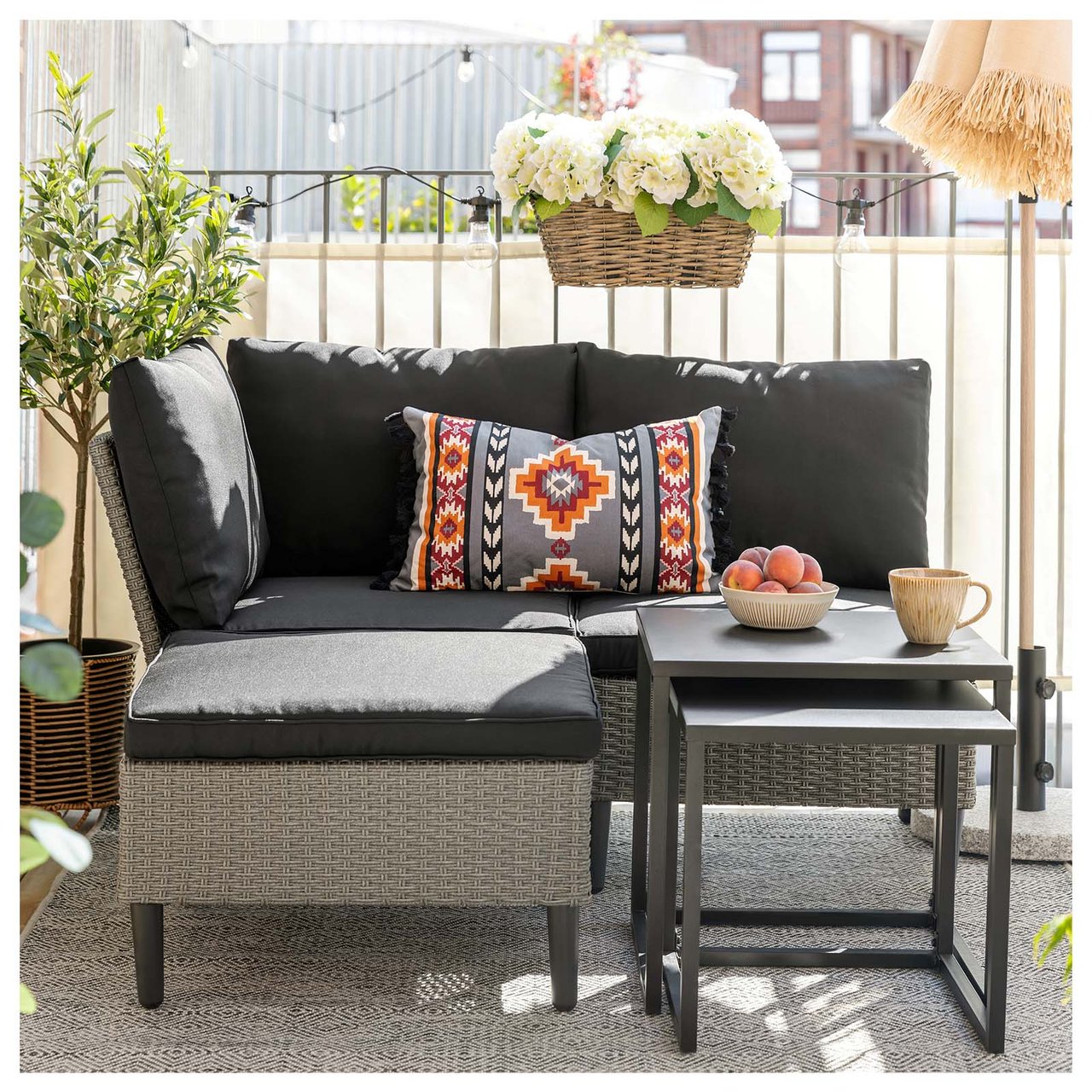 Hyggelig balkong med loungesofa i kunstrotting, lite settbord, planter og en parasoll.