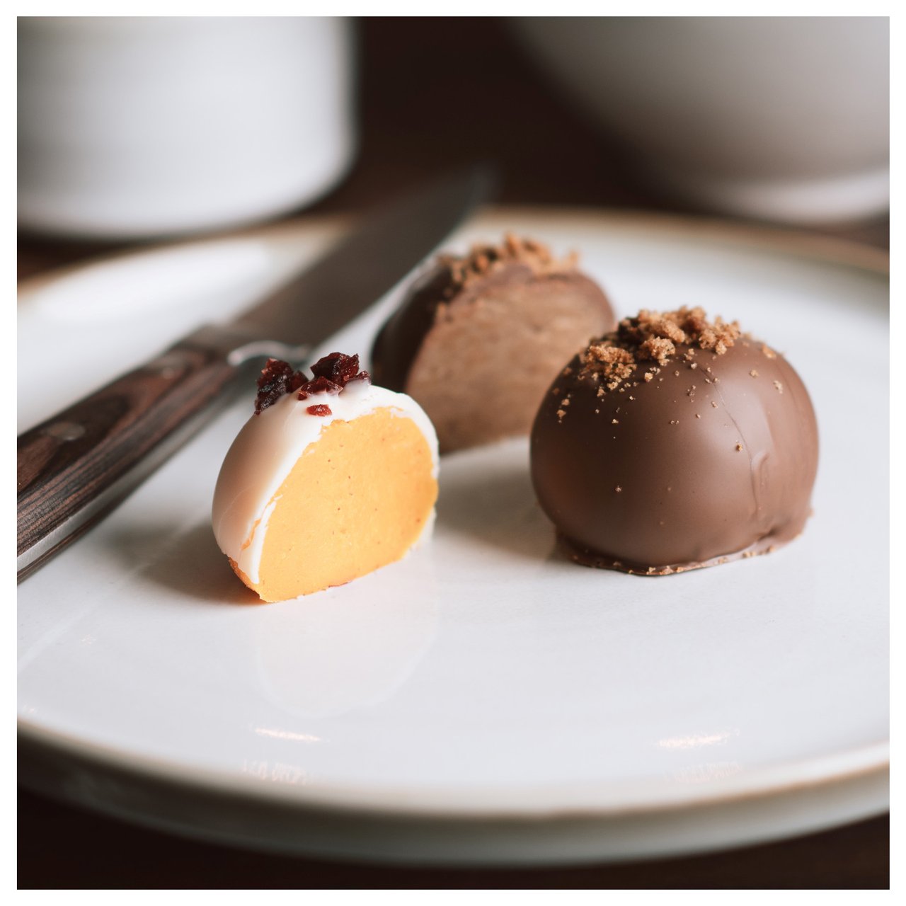 Kaksi valmista suklaakuorrutettua piparkakkupalloa on lautasella, toinen on halkaistu ja täyte näkyy.