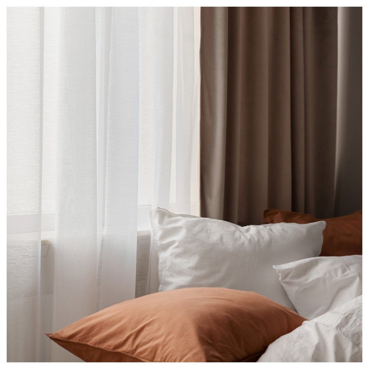 Kissen in einem gemachten Bett am Fenster mit transparenten Vorhängen und Verdunkelungsvorhängen.