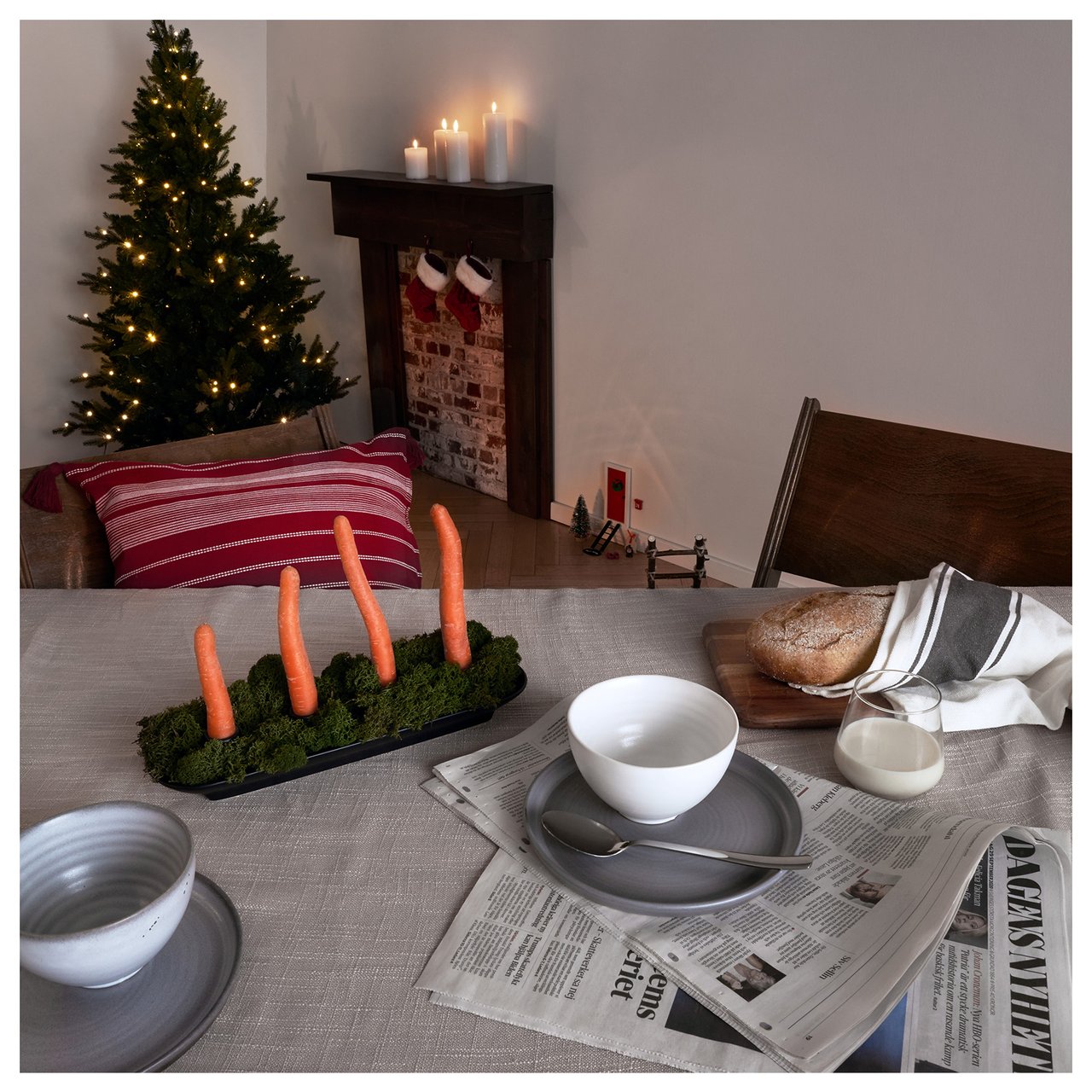 Vier Karotten im Adventsleuchter auf dem Frühstückstisch, im Hintergrund eine Wichteltür neben Kamin und Weihnachtsbaum.