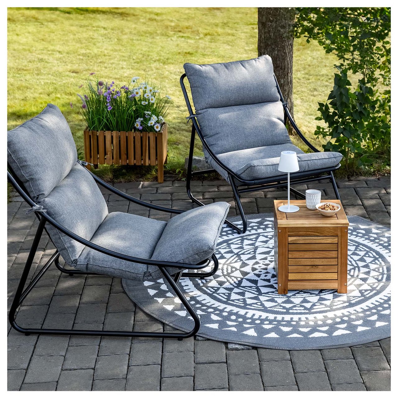 Zwei Entspannungsstühle mit rundem Sisalteppich und kleinem Beistelltisch auf einer Terrasse mit Steinplatten.