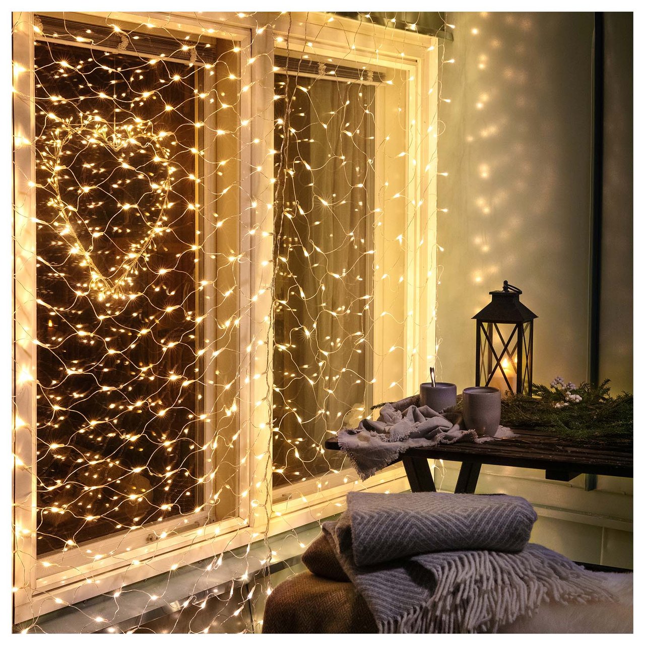 Fönster och uteplats dekorerade med ljusslingor, filtar och lykta i en varm kvällsmiljö.