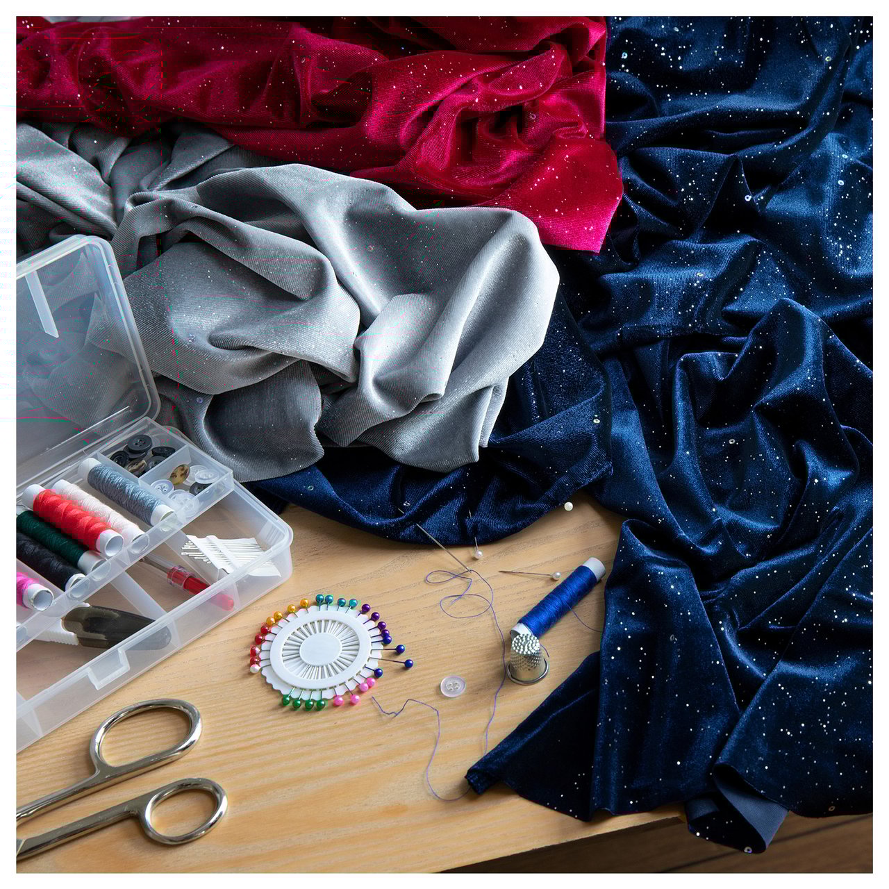 Ompelupöytä, jolla on kimaltelevia kankaita, lankarullia, neuloja ja saksia luoviin jouluaiheisiin tekstiilitöihin.