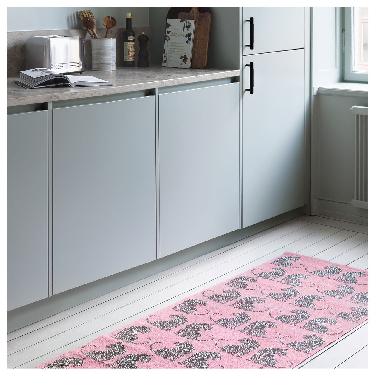 Et rosa teppe med tigre ligger på et kjøkkengulv. Bak ser man et stilrent kjøkken i grått.