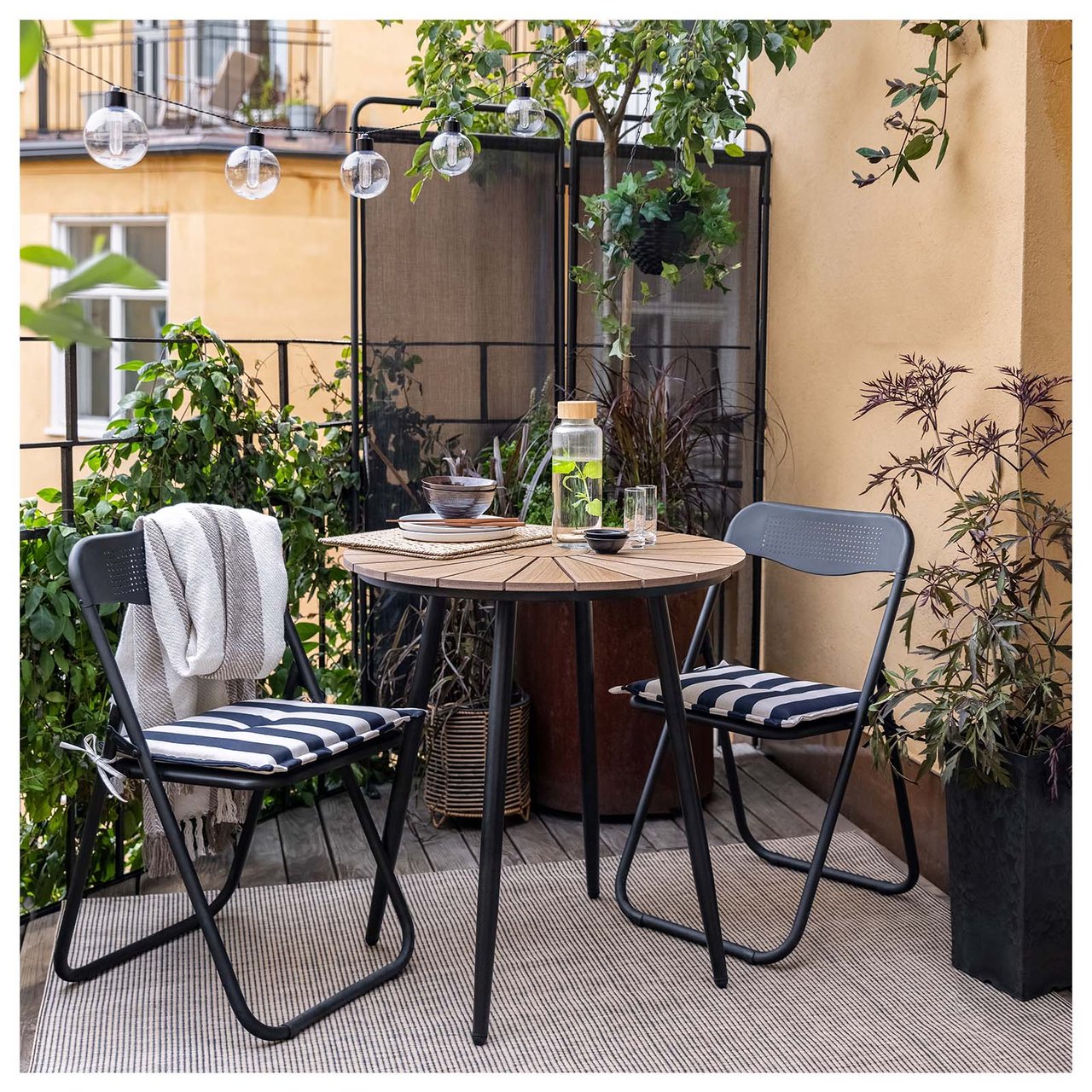 Beige teppe på en balkong sammen med svarte stoler og kafébord med svarte ben og treplate.