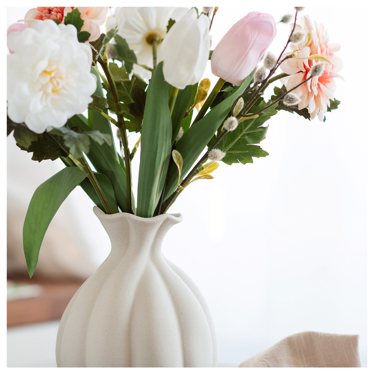 Beige Steingutvase mit pastellfarbenen, tulpenförmigen Kunstblumen und Hortensien als Nahaufnahme.