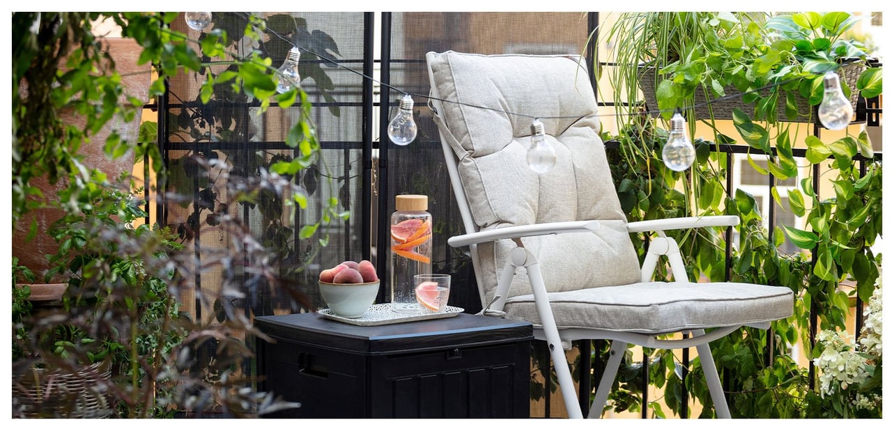 Gartenstuhl und kleiner Tisch auf dem Balkon mit Kletterpflanzen und Lichterkette am Balkongeländer.