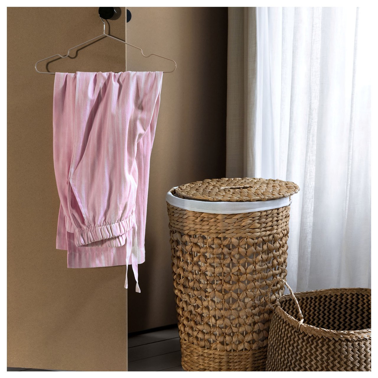 Rosa pysjamasbukser henger på en kleshenger ved siden av to oppbevaringskurver i naturfarger.