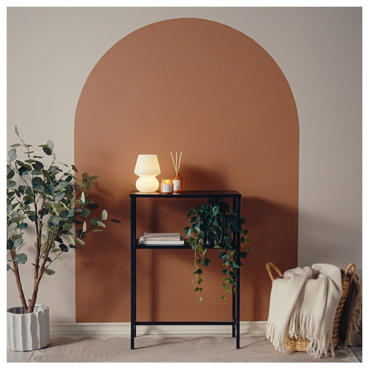 Avlastningsbord med lampe og plante foran en vegg med bue malt i kontrastfarge.