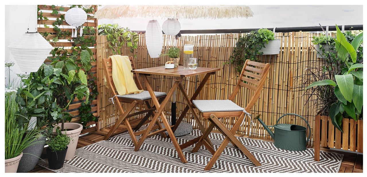 Mysigt hörn på balkong med två nätta stolar och bord inramas med utomhusmatta, växter och ljusslingor.