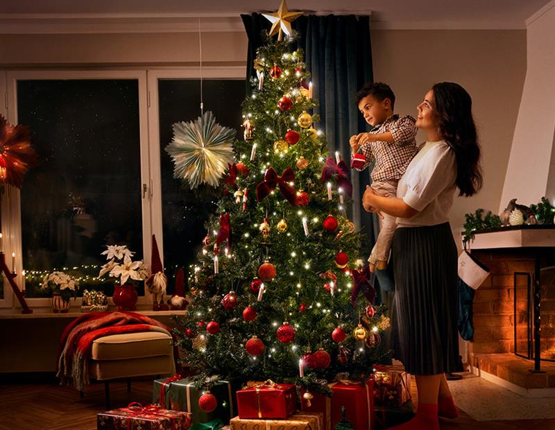 En voksen og et barn pynter juletreet sammen i en koselig stue.