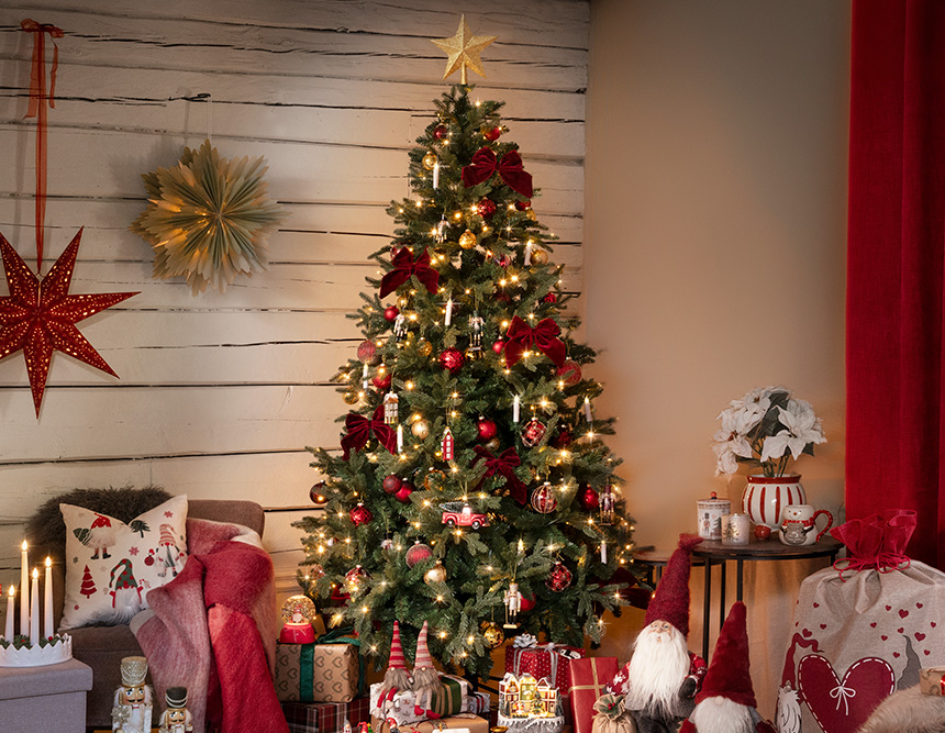 Et pyntet juletre står i en koselig stue omgitt av julegaver.