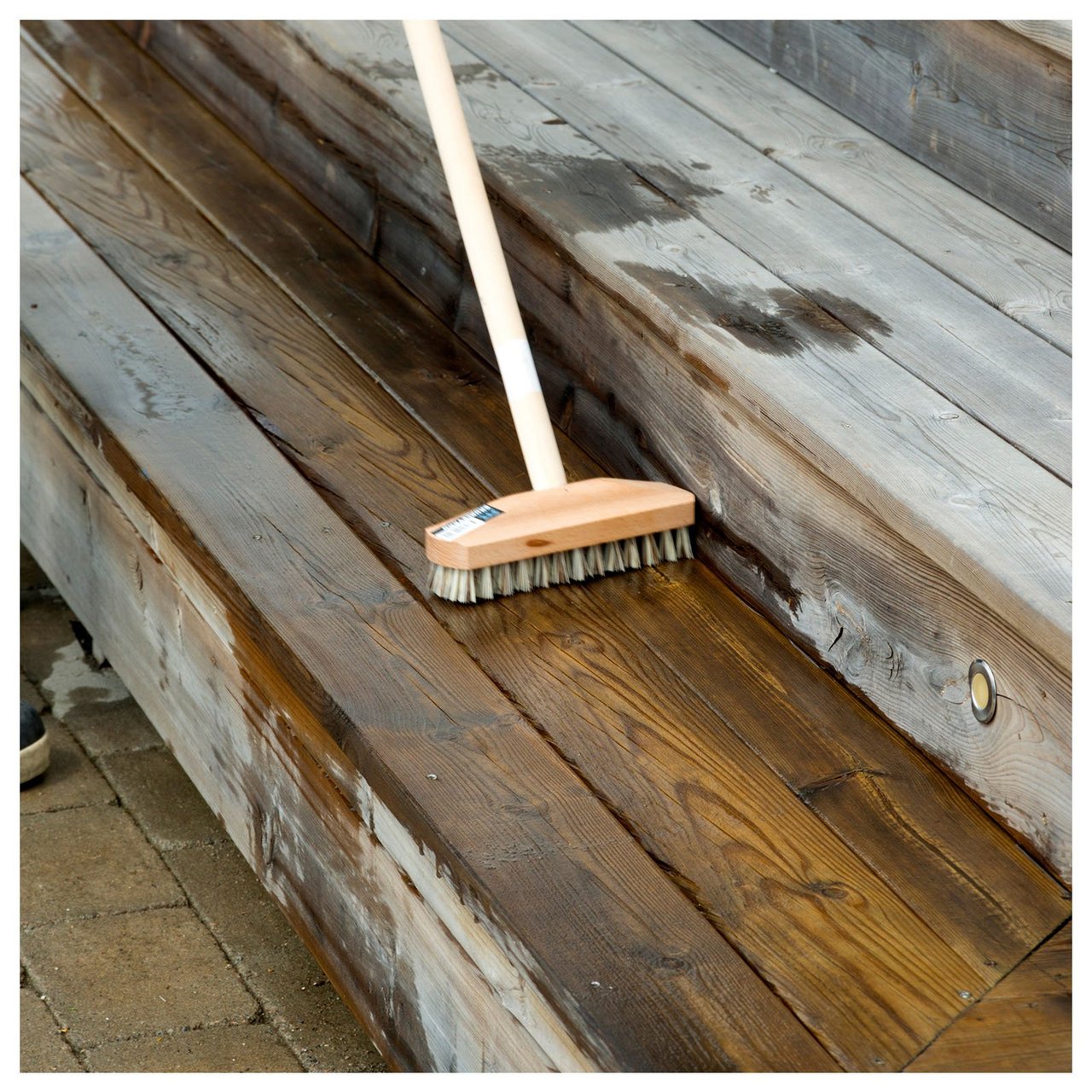 Eine Terrassentreppe aus Holz wird mit einer Bürste geschrubbt.