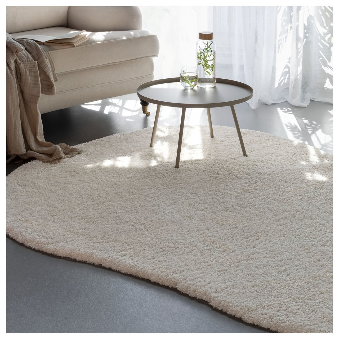 Organisch geformter weißer Teppich vor einem Sofa.