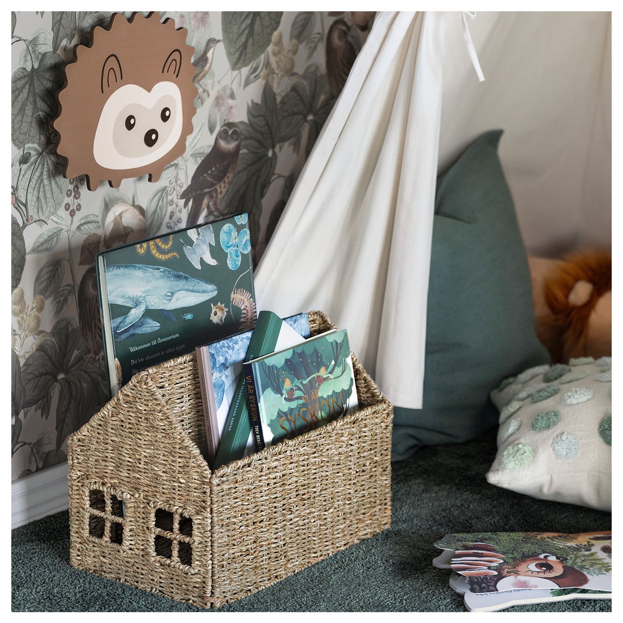 En del av ett barnrum där man ser en förvaringskorg för böcker i form av ett hus och en lampa i form av en igelkott.