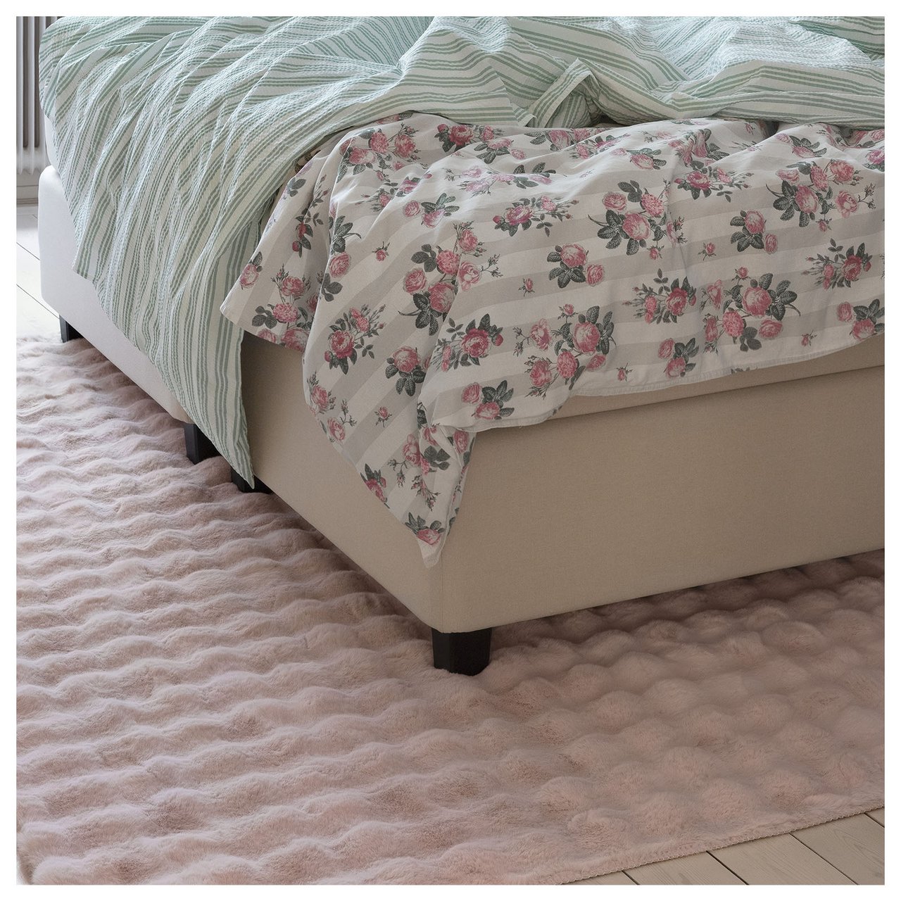 Soverom med rosa, mykt teppe og sengetøy i blomstermønster, rosa og grønne striper.