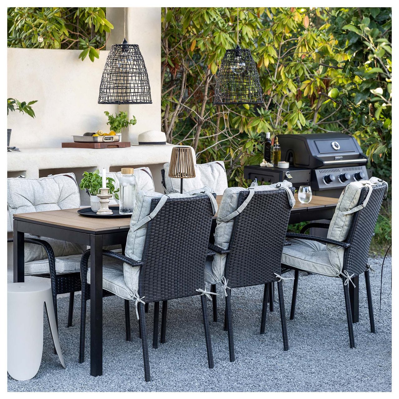 Eine Essgruppe aus vier Stühlen und einem Tisch steht auf einem Teppich im Garten, umgeben von hängenden Solarleuchten.