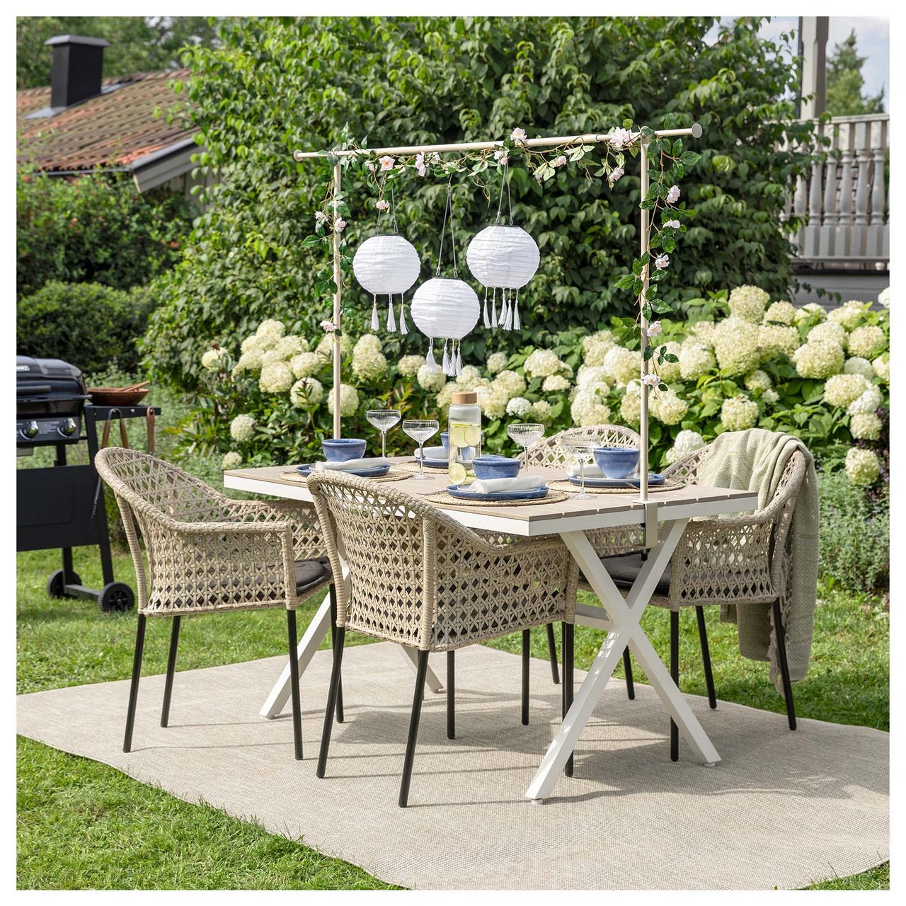 Eine Essgruppe aus vier Stühlen und einem Tisch steht auf einem Teppich im Garten, umgeben von hängenden Solarleuchten.