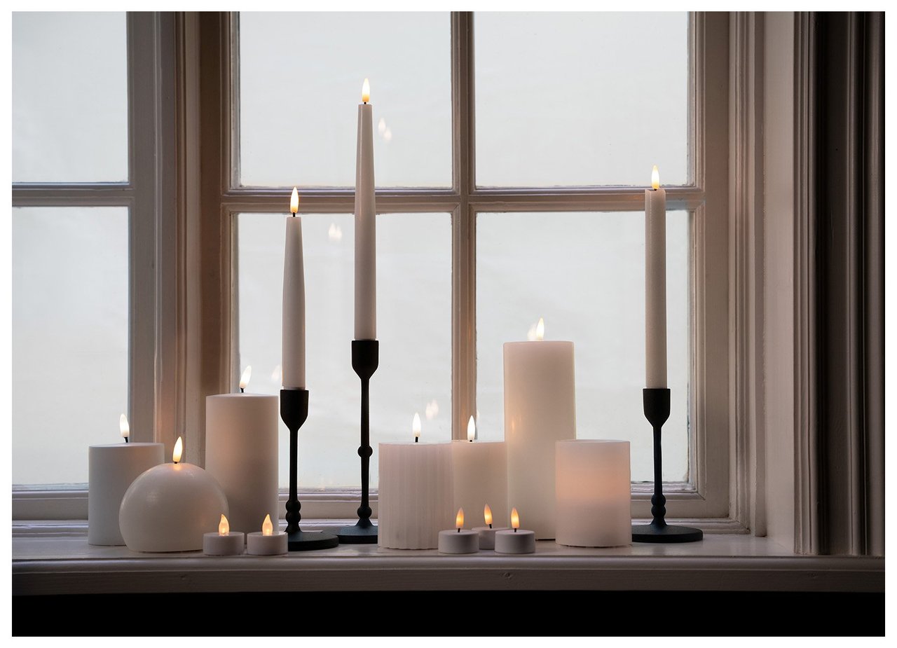 Fensterbrett, dekoriert mit mehreren angezündeten Stumpen- und Stabkerzen in verschiedenen Höhen und Kerzenhaltern.