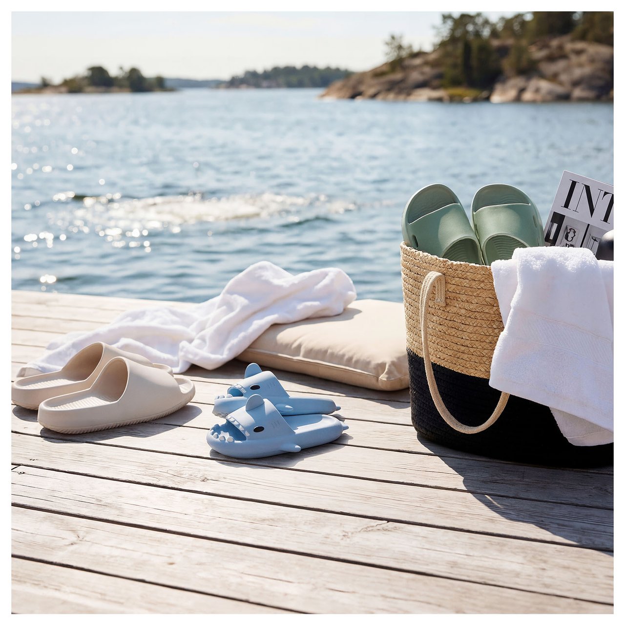 Bootssteg mit Badeschuhen und Strandtasche. Glitzerndes Wasser im Hintergrund.